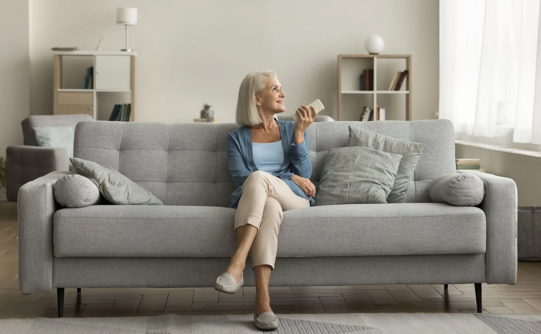 Mulher sentada no sofá com controle do climatizador - como fazer o climatizador gelar mais