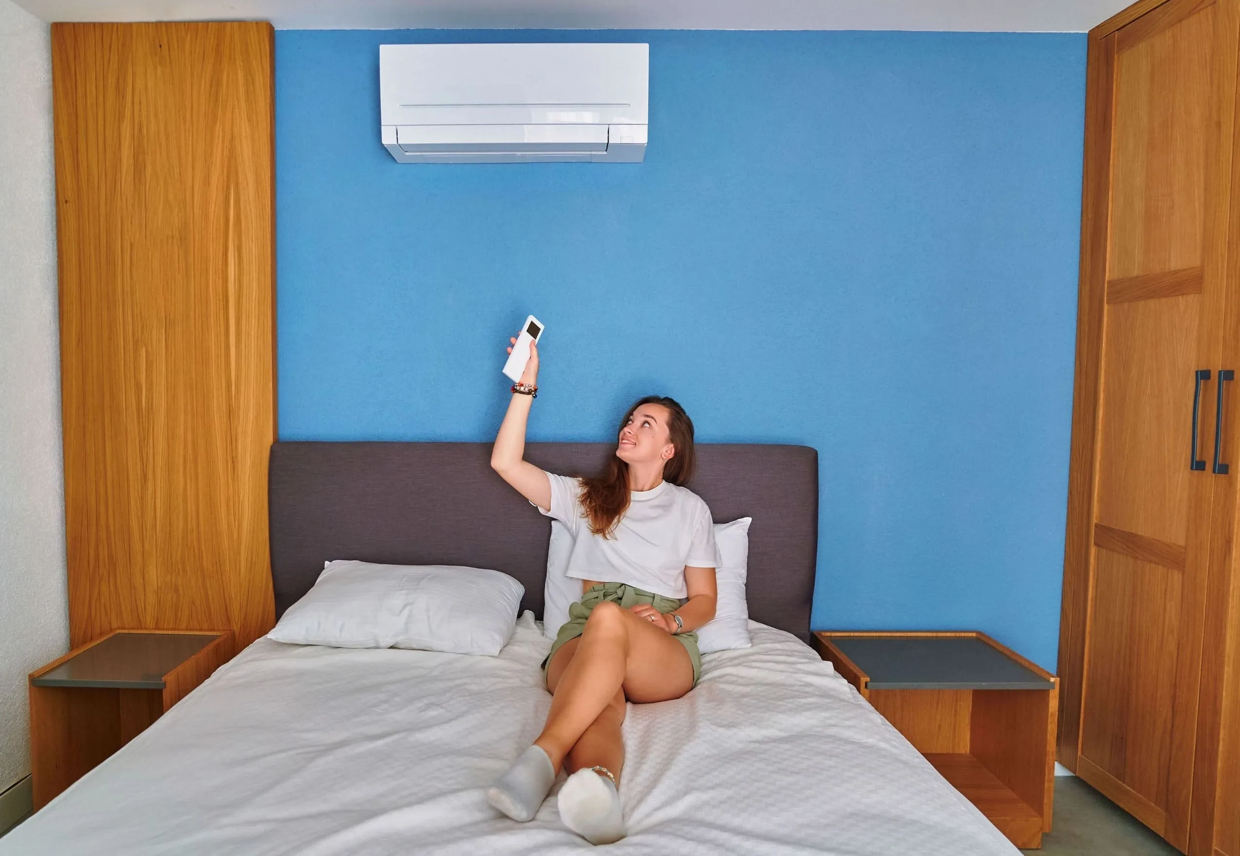 Mulher deitada na cama ligando ar-condicionado para espantar pernilongos